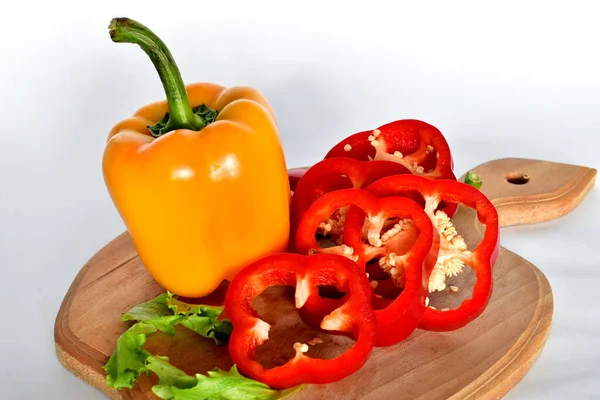 On the cutting board lies a Bulgarian red pepper cut into rings and one yellow whole fruit.