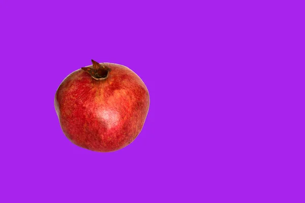 A round pomegranate fruit with juicy red grains lies on a purple background.