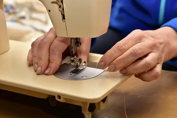 The picture shows the hands of a woman who inserts a bobbin of thread into the mechanism of a sewing machine.