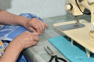 Dikiş makinesinin durduğu masada oturan terzi kumaşı dikiş için hazırlar..