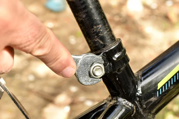 The hand of a locksmith who checks the tightening of a bolt with an open-ended locksmith's wrench on a bicycle frame bolt.