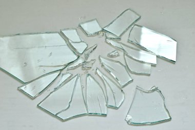 Kırık cam parçaları çeşitli şekil ve boyutlarda gri bir arka planda yatıyor..