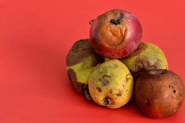 Rotten fruits, apples and pears lie on a pink background.