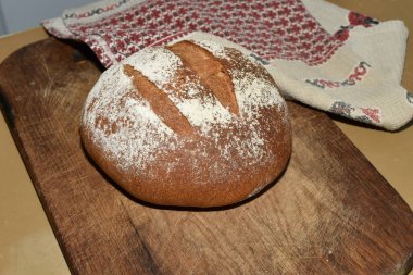 Bir kesme tahtasının üzerinde, evdeki mutfakta fırında pişirilmiş yuvarlak ekmek var..