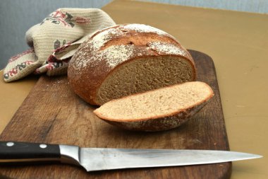 Yuvarlak ekmek kesme tahtasının üzerinde, somundan bir parça kesmek için kullanılan bıçağın yanında..