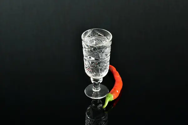 浓郁而透明的酒精倒入水晶玻璃中 红辣椒在黑暗的背景下躺在附近 — 图库照片