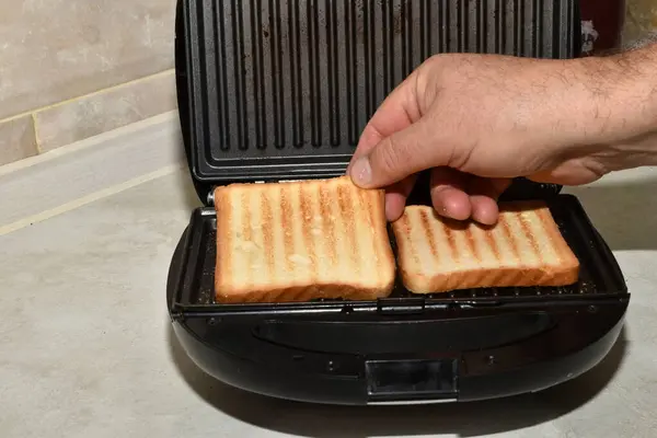 A mans hand removes ready-to-eat fried bread from a toaster.