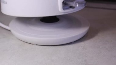 Bir adamın eli podyuma plastik bir su ısıtıcısı yerleştirir ve parmağıyla güç düğmesine basar..