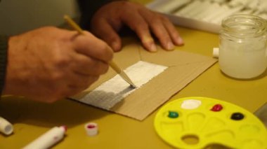 Bir adam masaya oturur ve beyaz boyayı karton bir fırçayla uygular..