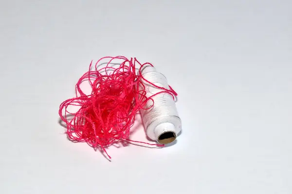Red threads and a spool of white threads isolated on a white background.