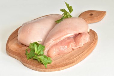 Beyaz arka planda, kesme tahtasının üzerinde pişmeye hazır çiğ tavuk göğsü var. Etlerin yanında defne yaprağı, biber ve sarımsak var..