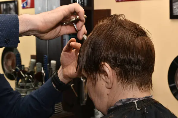 A hairdresser using a comb and scissors shortens the hair of a bang, side view.