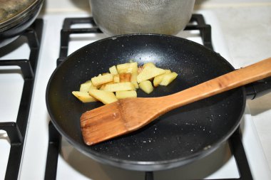 Kızarmış patatesli kızartma tavası ve gaz sobasının üzerinde duran ahşap bir spatula..