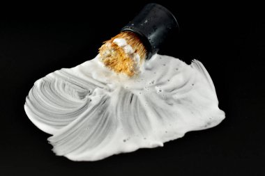 Siyah bir arka planda, tıraş köpüğü ve yüzeye bulaşmış eski bir tıraş fırçası..
