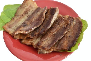 Resim, yeşil yaprakların üzerinde kızartılmış domuz pastırması parçalarını gösteriyor..