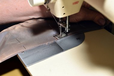 Dikiş makinesinde çalışan bir terzi, masada otururken kumaş dikiyor..