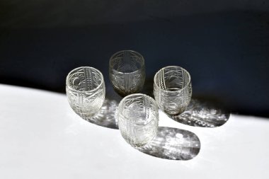 Beyaz ve siyah arka planda gölgelerin beyaz ve siyah arkaplana yansıtıldığı dört kristal bardak vardır..