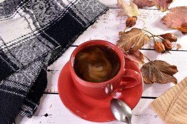 Düşen yapraklarla kaplı bir masada bir fincan sıcak çay ve sıcak bir eşarp var..