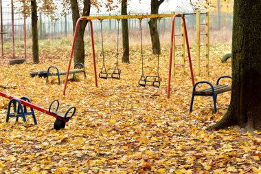 Sarı yapraklar, sonbaharda bir çocuk parkında atlıkarıncaların etrafındaki zemini kaplamıştı..