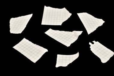 Küçük yırtık beyaz kağıt parçaları siyah arka plana saçılmış..