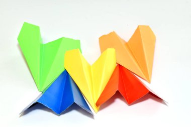 Farklı renklerde kağıt uçaklar beyaz arka planda yan yana uzanıyorlar..
