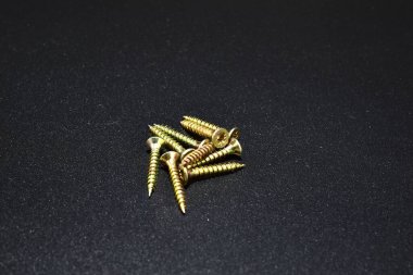 A group of wood screws lie on a black background. clipart