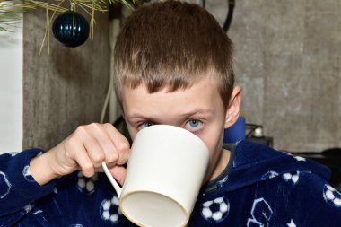 Çocuk beyaz bardaktan bir şey içiyor..