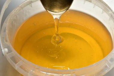 Kalın bal kaşıktan kovaya damlıyor, yakın plan..