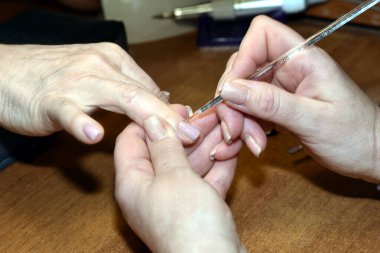 Manikürcü, müşterinin tırnaklarına fırçayla oje sürüyor..