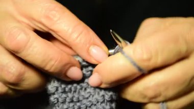 Kadın ellerinin örgü iğneleri ve yün ipliklerle bir şeyler ördüğü yakın plan..