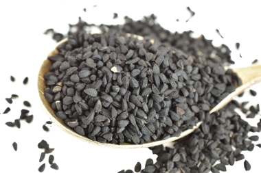 Siyah kimyon tohumları beyaz arka planda bir kaşıkta yatıyor..