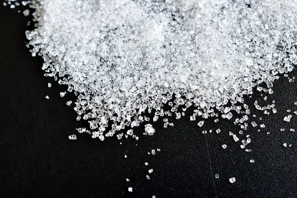 Şeffaf şeker kristalleri siyah arkaplana dağılmış..