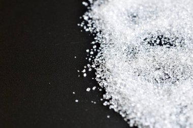 Beyaz şeker kristalleri siyah arkaplanda yatar.