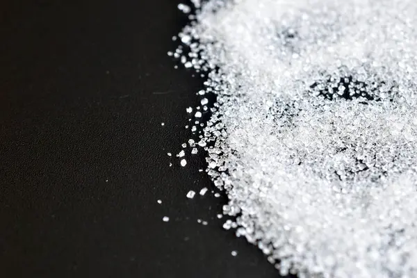 Beyaz şeker kristalleri siyah arkaplanda yatar.