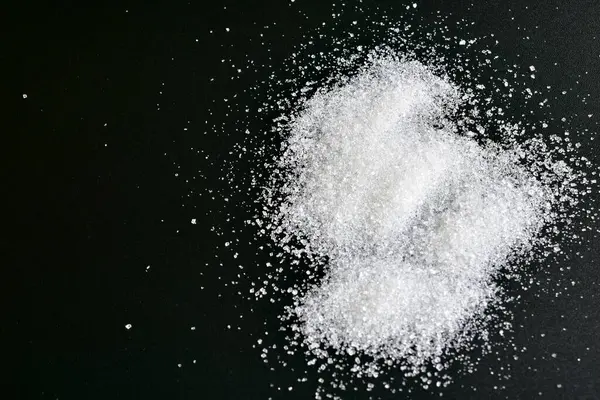 Beyaz şeker kristalleri siyah arkaplanda yatar.
