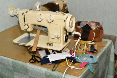 Terzinin çalışma masası. Masanın üzerinde dikiş makinesi, iğneler, makas ve kumaş parçaları var..