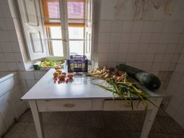 Çeşitli sebze ve meyvelerle dolu bir masa. Kabak da dahil. Masa, penceresi ve kapısı olan bir mutfakta.