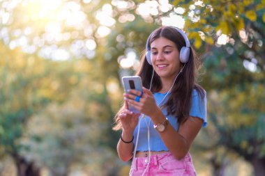 Otururken telefonuyla müzik dinleyen kulaklık takan bir kız..