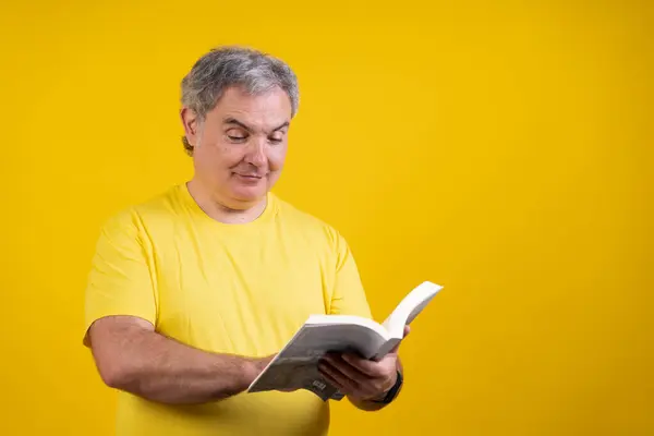 Sarı gömlekli bir adam kitap okuyor. Gülümsüyor ve kitaptan zevk alıyor.