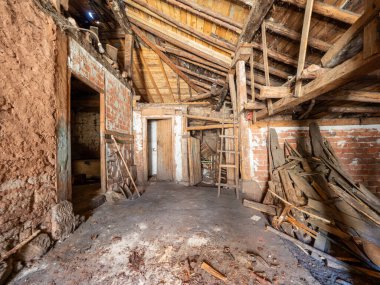 Yıkılan duvarlar ve dağınık döküntüler terk edilmiş bir çiftlik evinin içini dolduruyor, çürüyen durumunu ve ahşap çatısını vurguluyor.