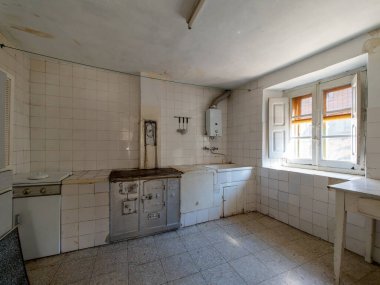 Terk edilmiş bir evde eski, çürüyen bir mutfak zamanın ve ihmalkarlığın bir göstergesi olarak duruyor. Eski aletler ve yıpranmış yüzeyler var.