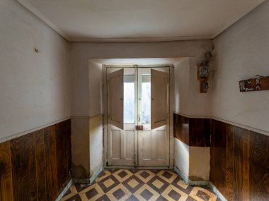 Sunlight entering through open door of abandoned house with vintage geometric tiled floor and wood paneling clipart