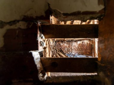 Güneş ışığı, hasarlı zemini aydınlatıyor ve terk edilmiş evin tavanındaki delikten dökülen tuğla duvarı yıkıyor.