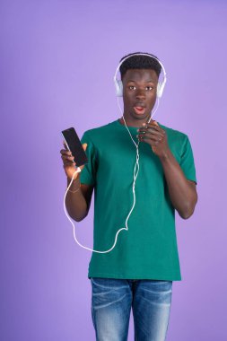 Kulaklık takan ve elinde akıllı bir telefonla mor bir arka planda müzik dinleyen genç bir adam.