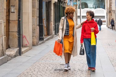 Alışveriş çılgınlığından sonra alışveriş torbaları taşıyan iki kız arkadaş birlikte yürüyüp sohbet ediyorlar.