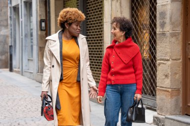 Cazibeli bir kaldırım taşı caddesinde yürüyen iki kadın mutlu bir şekilde el çantalarını tutarken neşeli bir sohbete daldılar.