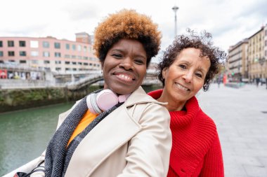 İki mutlu çoklu etnik kadın, Sinir Nehri ile birlikte Bilbao şehir merkezinde poz veriyorlar.