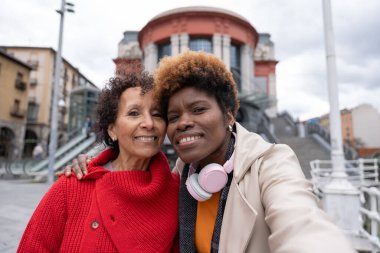 İki mutlu çoklu etnik kadın arka planda Arriaga tiyatrosuyla Bilbao şehir merkezinde selfie çekiyor.