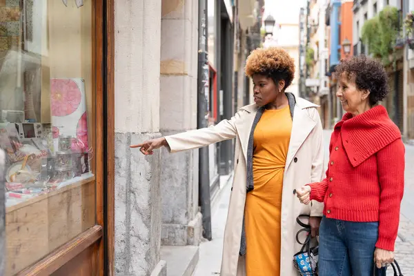 Caddede yürüyen, vitrinlere bakan ve vitrindeki ilginç eşyalara bakan iki kadın.