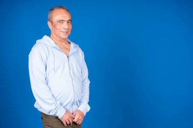 Canlı mavi bir arkaplanda poz verirken gülümseyen kendinden emin yaşlı bir adamın portresi.